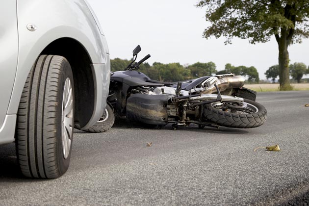 imagem e carro estacionado e moto caída à frente, indicando um acidente envolvendo os dois veículos