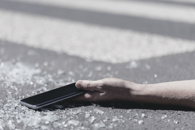 imagem de uma mão estendida no asfalto segurando um celular, após acidente de trânsito