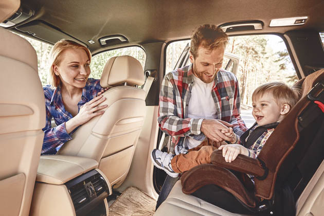 pai prendendo criança na cadeirinha do carro enquanto a mãe observa no banco do carona