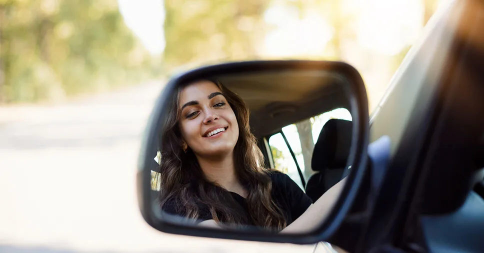 mulher sorridente manobrando o carro com facilidade sabe a importância do espelho retrovisor